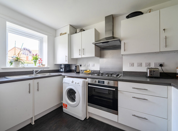 Modern fitted kitchen with white units, sink, oven, washing machine and window over the worktop