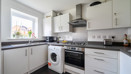 Modern fitted kitchen with white units, sink, oven, washing machine and window over the worktop