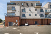 Back of an apartment building with balconies and a parking area.