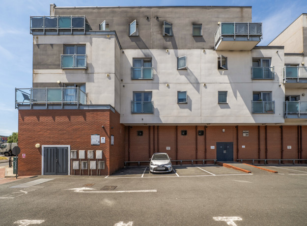 Back of an apartment building with balconies and a parking area.