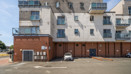 Back of an apartment building with balconies and a parking area.