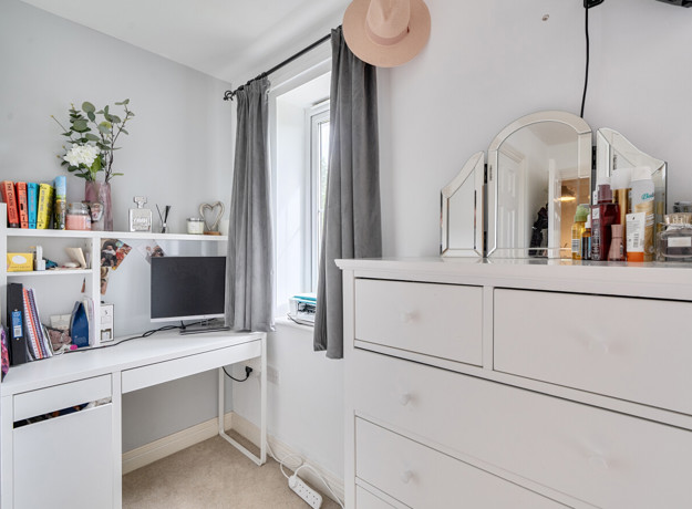 Room with white dresser, mirror, desk and shelving unit beside a window.