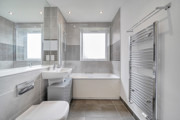 Contemporary bathroom with bathtub, overhead shower, toilet, sink, and grey wall tiles