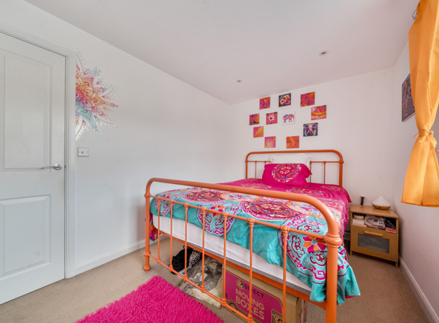 Bedroom with a single bed, colourful bedding, neutral décor, and window providing natural light.