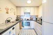 Galley kitchen with white cabinets, tiled floor and appliances