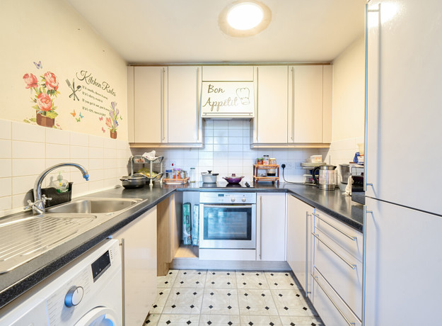 Galley kitchen with white cabinets, tiled floor and appliances