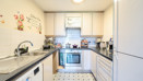 Galley kitchen with white cabinets, tiled floor and appliances