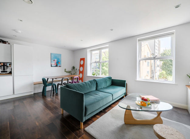 Open-plan living room with a teal sofa, dining table and large windows.