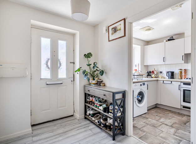 Entry hallway with a door, shelving unit and access to the kitchen.
