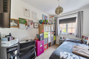 Bedroom with bed, desk, shelving and window with curtains.