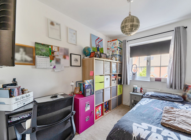 Bedroom with bed, desk, shelving and window with curtains.