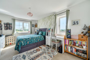 Bedroom with double bed, shelving unit and windows with curtains.