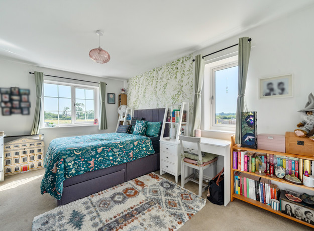 Bedroom with double bed, shelving unit and windows with curtains.