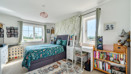 Bedroom with double bed, shelving unit and windows with curtains.