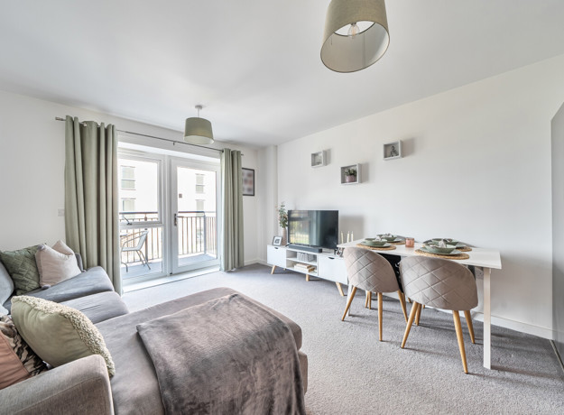 Open-plan living and dining area with sofa, dining table and balcony doors.