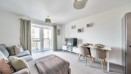 Open-plan living and dining area with sofa, dining table and balcony doors.