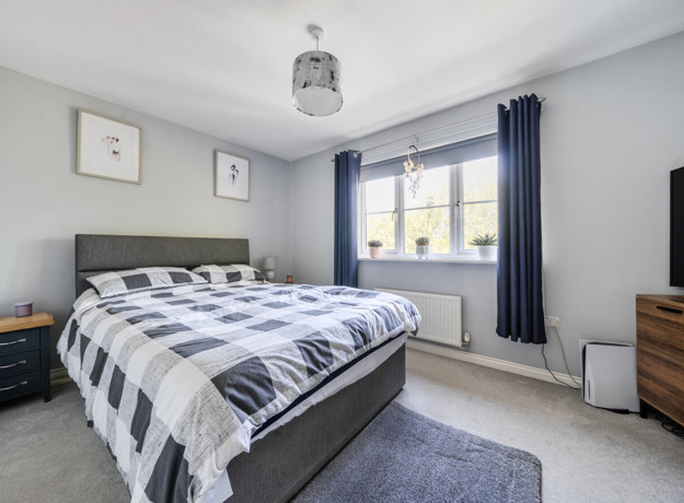 Bedroom with double bed, chest of drawers, and window with curtains.
