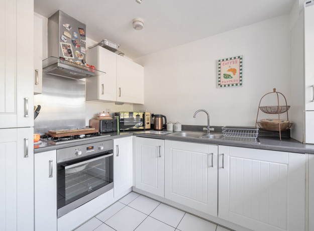 White fitted kitchen with integrated oven, hob and tiled flooring.