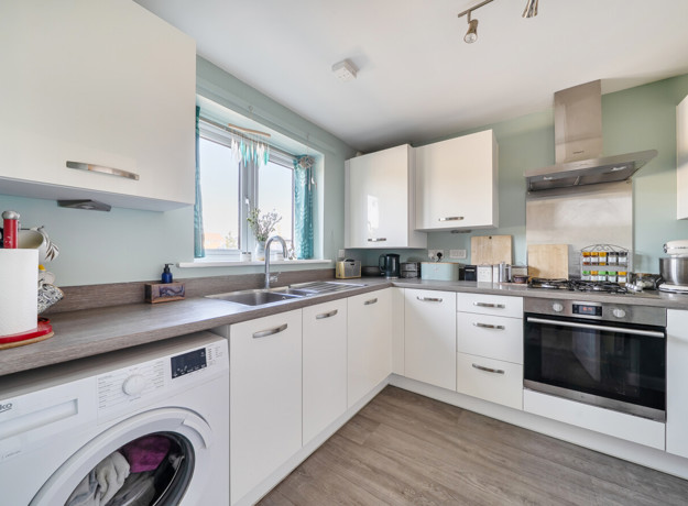 White fitted kitchen with integrated appliances and wood-effect flooring.