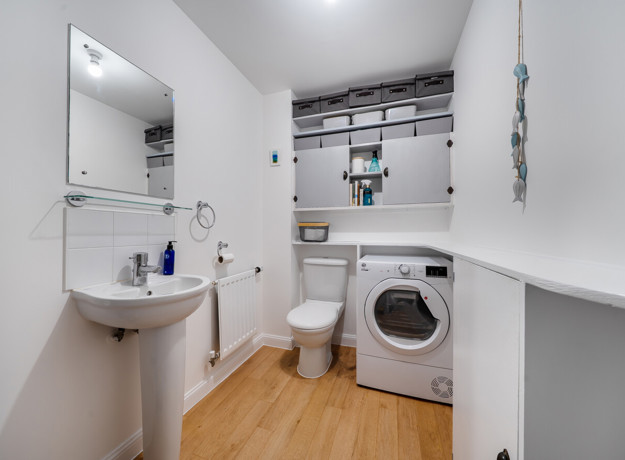 Utility room with sink, washing machine, storage shelves and worktop.
