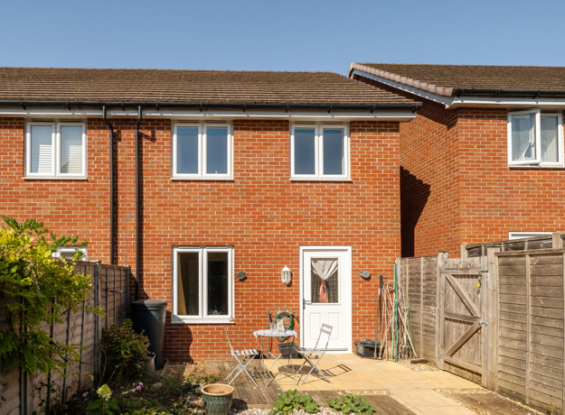 Rear view of a red brick house with patio doors and enclosed garden.
