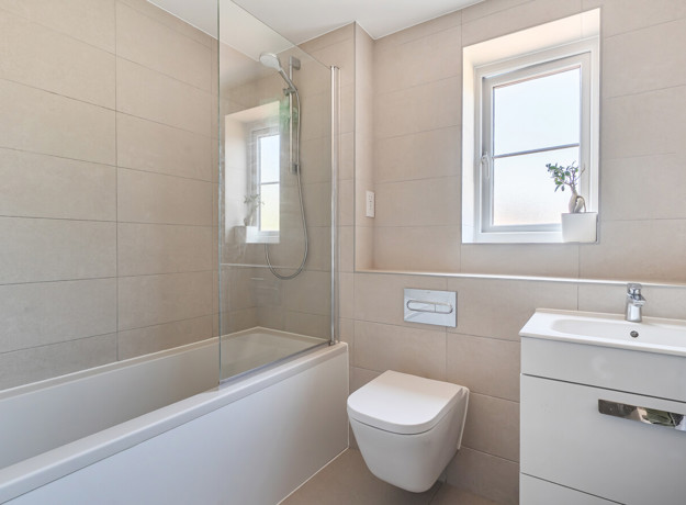 Bathroom with bathtub, shower screen, toilet, sink and frosted window.