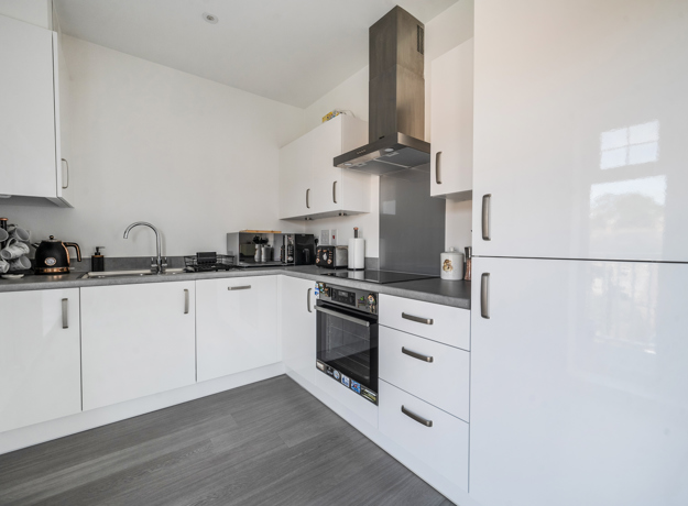 Kitchen with white cabinets, oven, hob, sink and appliances along walls.