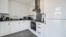 Kitchen with white cabinets, oven, hob, sink and appliances along walls.