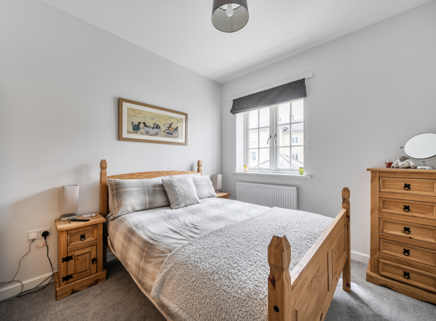 Bedroom with wooden bed frame, drawers, and window with blinds.