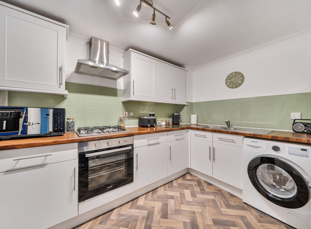 Kitchen with fitted cabinets, oven, washing machine and worktops.