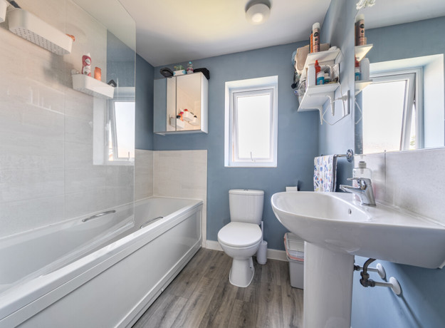 Bathroom with bathtub, toilet, sink, wood-effect flooring and blue painted walls.