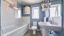 Bathroom with bathtub, toilet, sink, wood-effect flooring and blue painted walls.