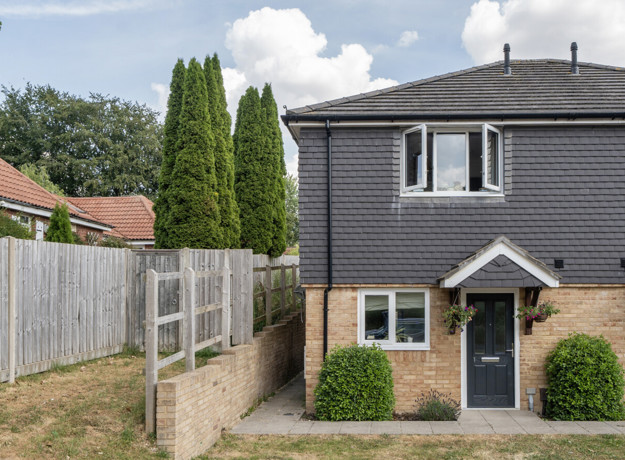 A two-storey semi-detached house with a fenced side path and shrubs.