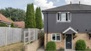 A two-storey semi-detached house with a fenced side path and shrubs.