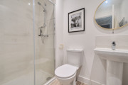 Ensuite with glass shower, toilet, sink, and round mirror.