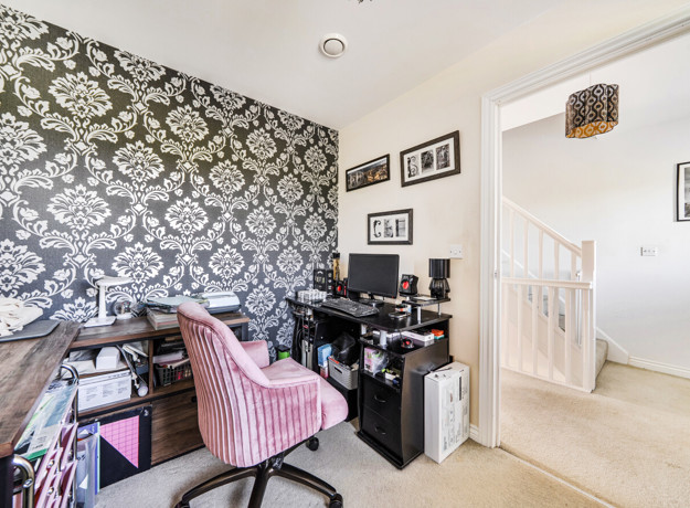 Home office with desk, chair, patterned feature wall and light carpet