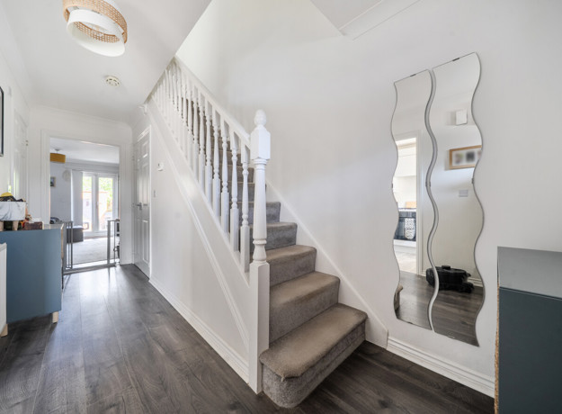 Hallway with staircase, wall mirror, and wood-effect flooring.