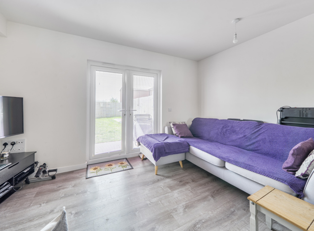 Living room with a purple sofa, TV and patio doors to the garden.