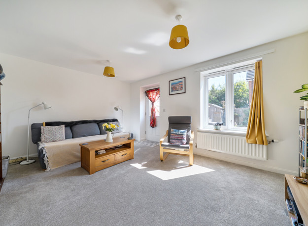 Living room with sofa, shelving, television and patio door to the garden.