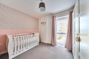 Nursery room with cot, patterned feature wall,wardrobe and large window.
