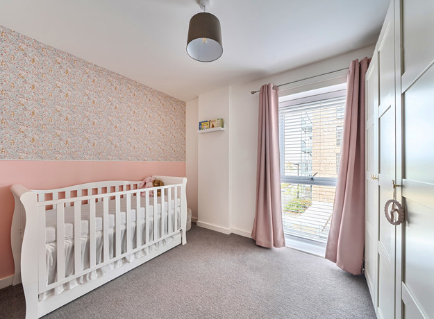 Nursery room with cot, patterned feature wall,wardrobe and large window.