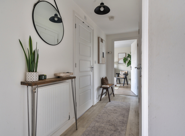 Hallway with console table, mirror, plant, and open doorway to living space.