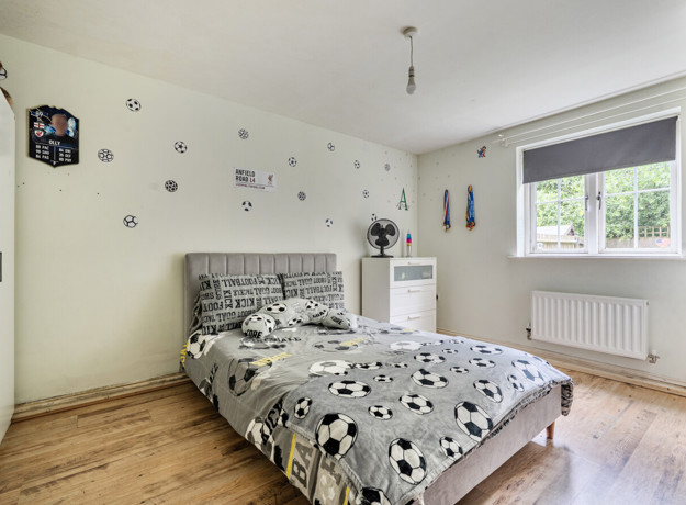 Bedroom with patterned bedding, window, radiator and light walls.