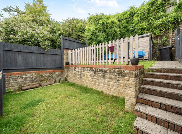 Terraced back garden with grass lawn, steps, retaining wall and shed.