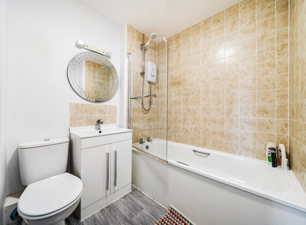 Bathroom with tiled walls, bathtub with shower, toilet and vanity unit