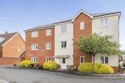 Modern red brick apartment building with white trim and small landscaped shrubs.