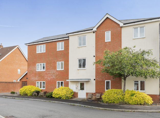 Modern red brick apartment building with white trim and small landscaped shrubs.