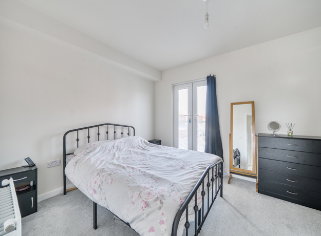 Bedroom with metal bed frame, chest of drawers and freestanding mirror.