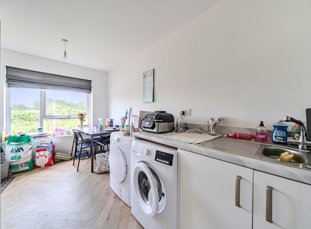 Kitchen with appliances, worktops, dining table with chairs and window.