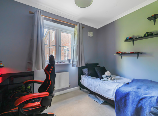 Single bedroom set up with bed, desk, shelving and window overlooking neighbouring buildings